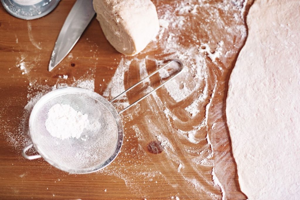 Top view of dough preparation with flour and kitchen tools.